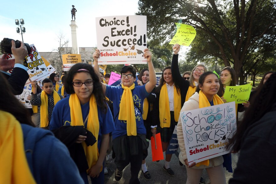 People wearing yellow scarfs hold signs in support of school choice. 