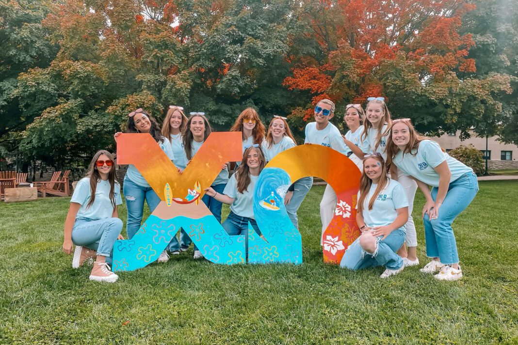 A group of people cluster around two giant Greek letters that spell out Chi Omega.