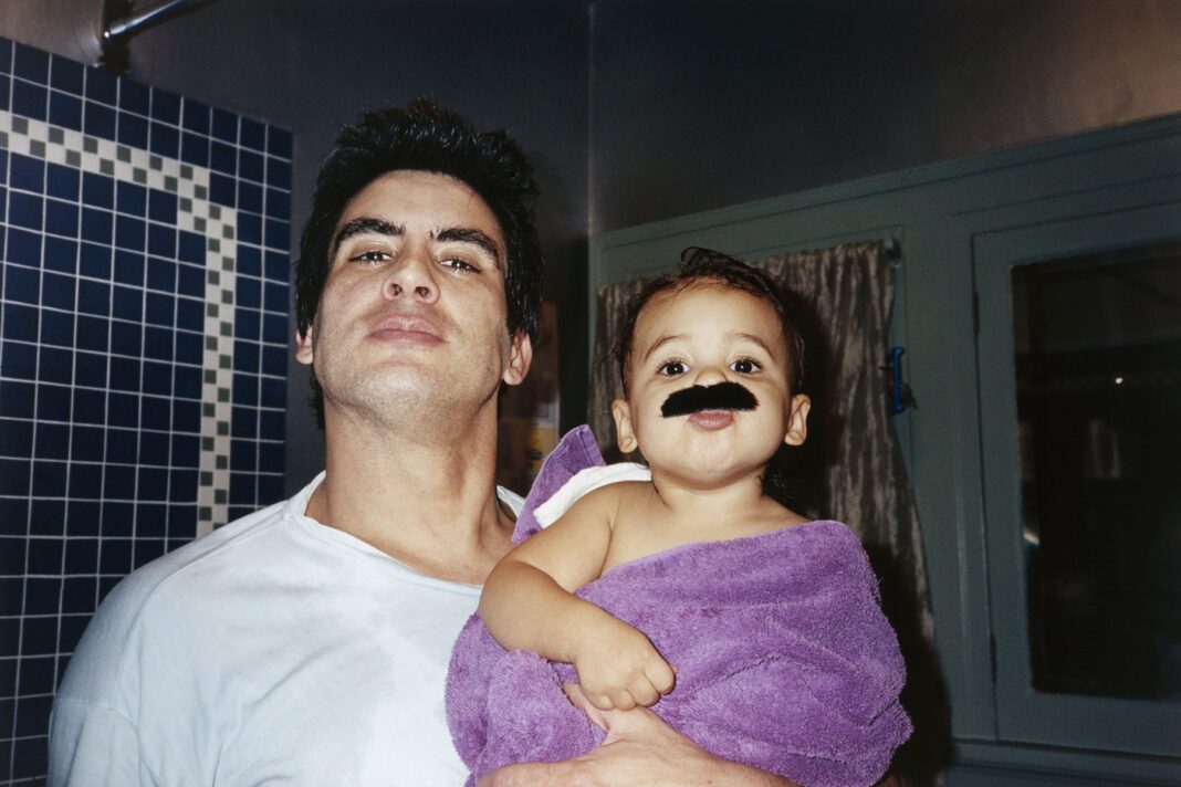 A dad and his child share a moment after a bath. The baby is wearing a fake mustache.